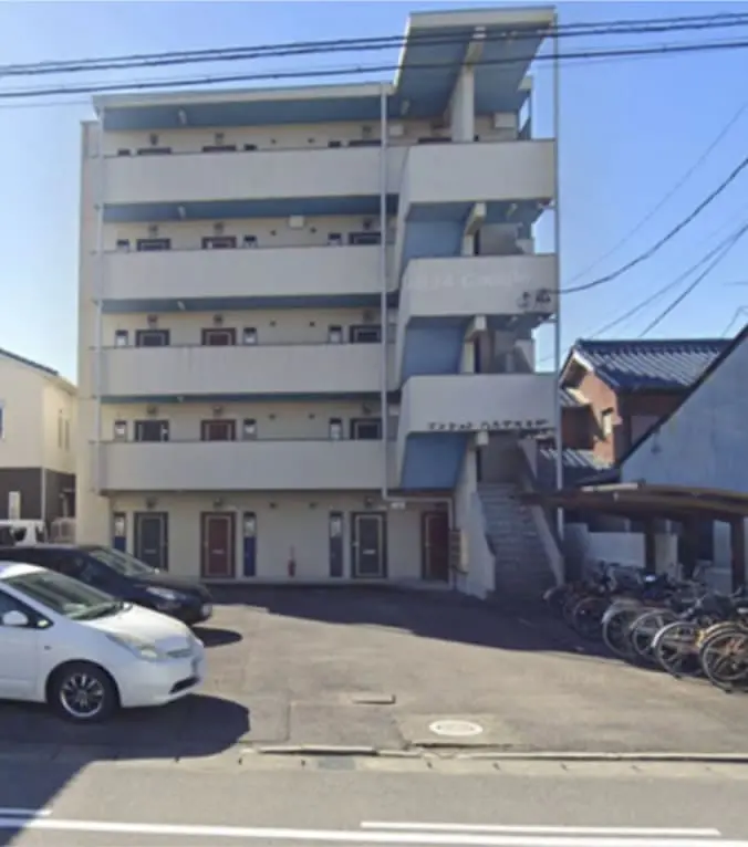 4〜5階建てのアパート型集合住宅で、建物前には駐車場と駐輪場があり、生活感のある街並み
                                                