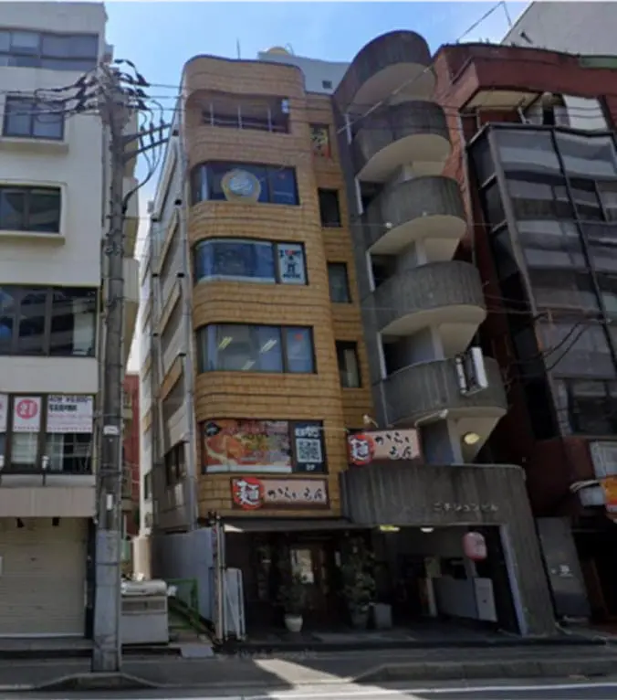 飲食店が1階に入った雑居ビルの外観で、看板やメニューが目立ち、商業地域の雰囲気がある
                                                