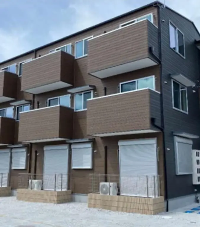 新築または築浅の低層アパートで、茶系の外壁と大きなバルコニーが整然と並ぶ外観
                                                